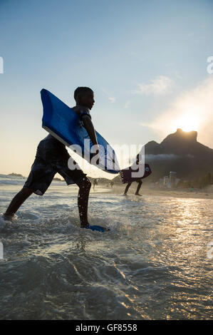 RIO DE JANEIRO - mars 8, 2016 : marche sur São Conrado Bodyboarders plage sous un coucher de soleil silhouette de l'emblématique Pedra da Gávea. Banque D'Images