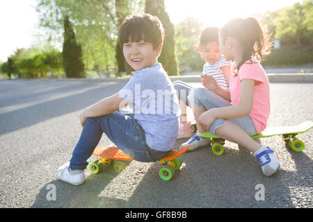 Heureux les enfants chinois assis sur une planche à roulettes Banque D'Images