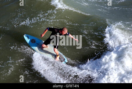 Un surfeur, tire le meilleur parti de la forte brise et une mer formée en début de soirée sur la plage de Brighton par l'épi à l'ouest de la jetée de Brighton (Palace Pier) Banque D'Images