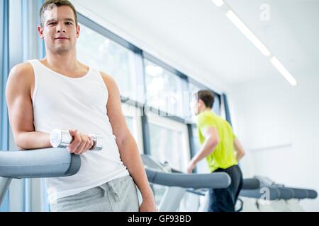 Parution de la propriété. Parution du modèle. Portrait of young man holding dumbbells tout en s'appuyant sur tapis roulant. Banque D'Images