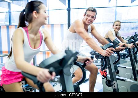Parution de la propriété. Parution du modèle. Les jeunes hommes et femmes qui travaillent sur des machines d'exercice dans la salle de sport, de sourire. Banque D'Images