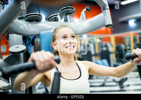 Parution de la propriété. Parution du modèle. Jeune femme faisant presse pectorale avec machine d'exercice dans la salle de sport. Banque D'Images