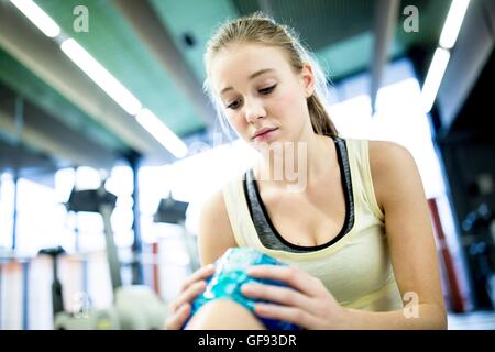 Parution de la propriété. Parution du modèle. Young woman holding paquet de glace sur le genou blessé dans une salle de sport. Banque D'Images