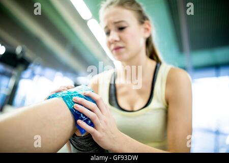 Parution de la propriété. Parution du modèle. Young woman holding paquet de glace sur le genou blessé dans une salle de sport. Banque D'Images