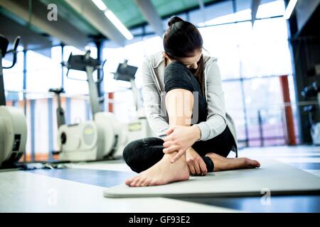 Parution de la propriété. Parution du modèle. Jeune femme tenant la cheville cheville tout en ayant des douleurs dans une salle de sport. Banque D'Images