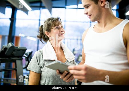 Parution de la propriété. Parution du modèle. Young man holding digital tablet et senior woman smiling in gym. Banque D'Images