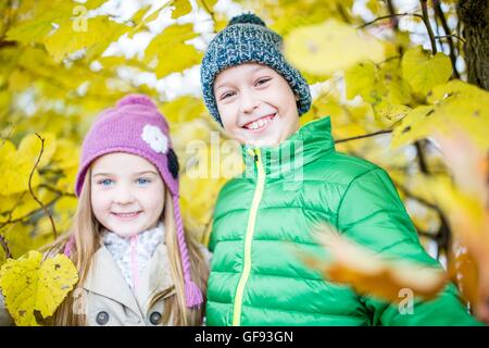 Parution du modèle. Les enfants debout à côté des plantes d'automne et souriant, portrait. Banque D'Images