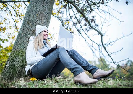 Parution du modèle. Jeune femme assise au tronc de l'arbre et à l'aide d'ordinateur portable. Banque D'Images