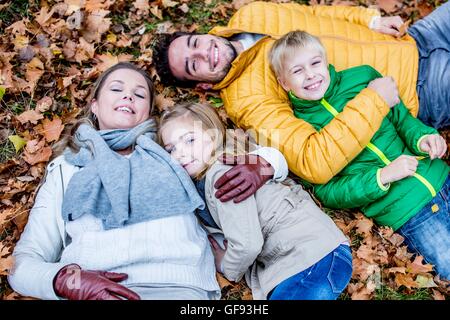 Parution du modèle. Famille étendu sur les feuilles séchées en automne et smiling, portrait. Banque D'Images