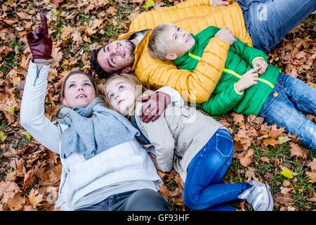 Parution du modèle. Famille étendu sur les feuilles séchées en automne et souriant, de la mère vers le haut. Banque D'Images