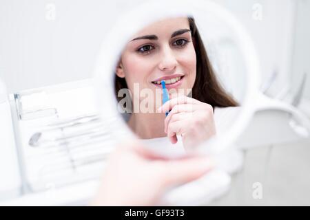 Parution du modèle. Jeune femme à l'aide de brosse interdentaire, tandis que la réflexion de miroir à l'hôpital. Banque D'Images