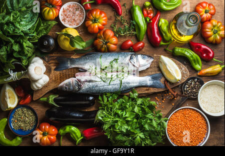 Le bar avec des poissons crus crus les légumes, les céréales, les herbes et épices sur planche à découper sur fond de bois rustique Banque D'Images