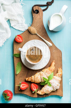 Le petit-déjeuner ou un dessert. Des croissants frais avec des fraises, une tasse de café et de lait en bouteille sur brown wooden board Banque D'Images