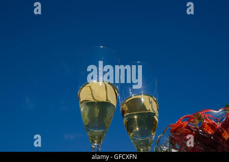 Deux verres de champagne et une partie d'un bol de fraises à l'extérieur dans un jardin par un ciel bleu Banque D'Images