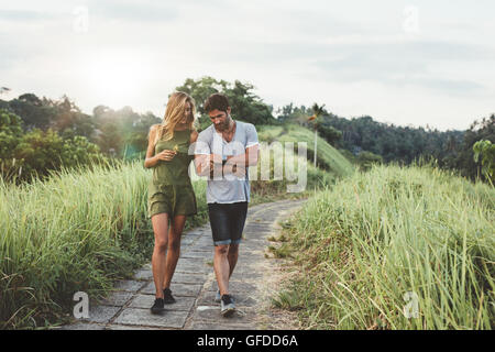 Young couple holding hands and walking through pathway in rural field. L'homme et de la femme marchant le long tall grass field. Banque D'Images