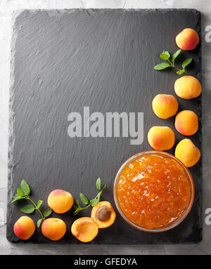 Confiture d'abricot dans un bol en verre, abricots frais sur fond noir en noir (vue du dessus ) Banque D'Images