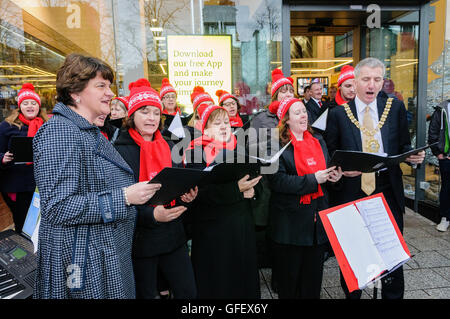 Belfast, Irlande du Nord. 12 Dec 2013 - Le ministre de l'Industrie et du Commerce, Arlene Foster, et Lord Maire de Belfast, Máirtín ó Muilleoir, chanter des chants de Noël à l'extérieur de la nouvelle £1.82M Belfast Welcome Center, un centre d'information touristique pour les visiteurs de Belfast et l'Irlande du Nord. Banque D'Images