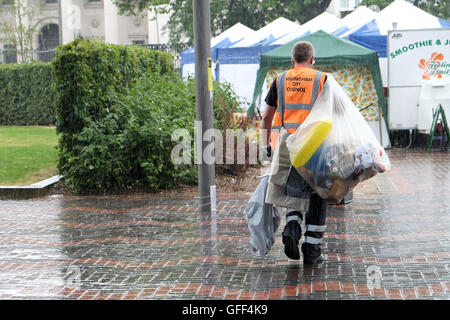 Un travailleur du Conseil dissipe sacs de détritus lors d'une pluie d'été soudaine tempête dans un centre ville animé salon Banque D'Images