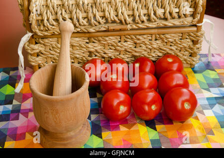 Les tomates empilées contre un panier tissé avec du mortier et pilon Banque D'Images