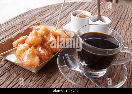 Bâtonnets de pâte frits dans une assiette en carton et l'ancien café sur la table en bois dans un matin Banque D'Images