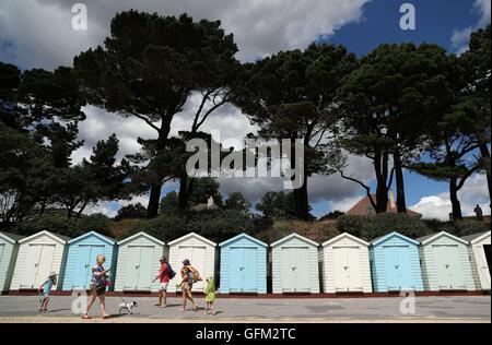 Les gens passent devant des cabines de plage sur Avon Beach de Mudeford, Dorset. Banque D'Images