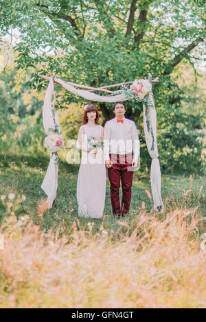 Élégant magnifique happy Bride and Groom standing près de l'arche de bois blanc pour une cérémonie de mariage Banque D'Images