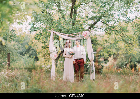 Jeune couple de jolie femme en robe de mariée et se toilettent standing in forest décorées de fleurs Banque D'Images