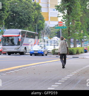 Un homme avec parapluie traverse road dans le quartier de Bugis à Singapour. Banque D'Images