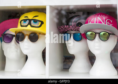 Des têtes de mannequin portant des casquettes et des lunettes de soleil sont exposées dans la fenêtre du magasin à Swanage, Dorset, Royaume-Uni Banque D'Images