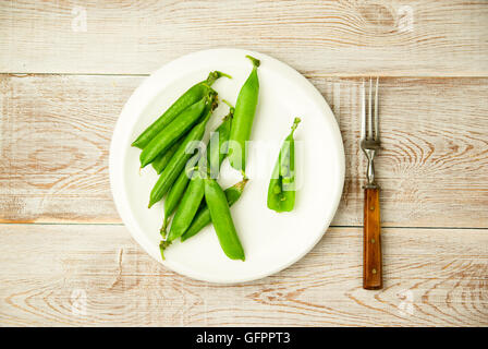 Les gousses de pois verts et la fourche sur la plaque blanche. Banque D'Images