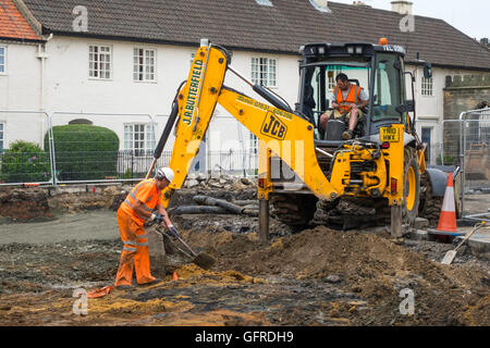 Workman à l'aide d'une excavatrice JCB re- pose d'une route, dans un site du centre-ville Banque D'Images