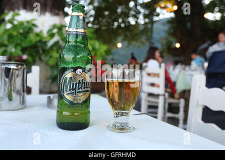 Bouteille et verre de bière Mythos sur table dans une taverne à Taxiarches square, le village de Tsagarada, Pelion, Grèce continentale. Banque D'Images