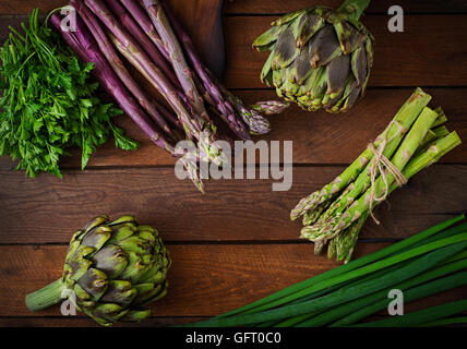 Les asperges et les artichauts avec des herbes sur un fond de bois. Vue d'en haut Banque D'Images