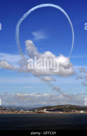 L'équipe des flèches rouges au-dessus de la mer avec une fumée blanche 360 contre un ciel bleu de Mumbles Hill avec la ville en arrière-plan Banque D'Images