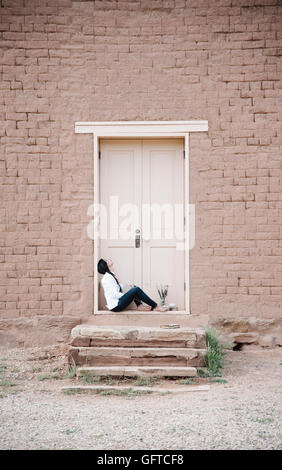 Jeune femme aux longs cheveux bruns assis sur le sol devant la porte d'un bâtiment Banque D'Images