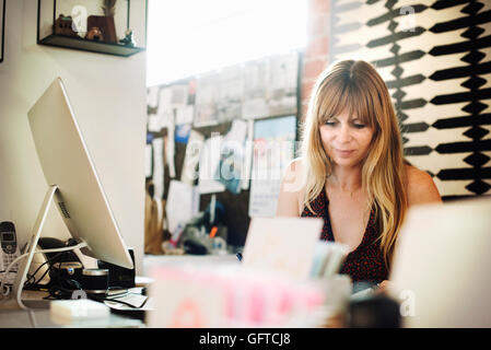 Femme assise dans un bureau à un bureau avec un ordinateur qui fonctionne Banque D'Images