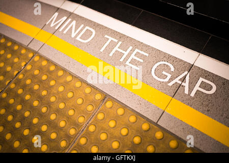 Mind the Gap inscription peinte sur le bord de la plate-forme de la gare, conceptuel, vignette assombrir edge, la profondeur de champ sur fond flou Banque D'Images