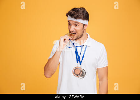 Gros plan du beau jeune homme sportif de mordre sa médaille sur fond jaune Banque D'Images