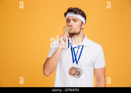 Portrait de jeune drôle spotrsman article et d'embrasser sa médaille sur fond jaune Banque D'Images