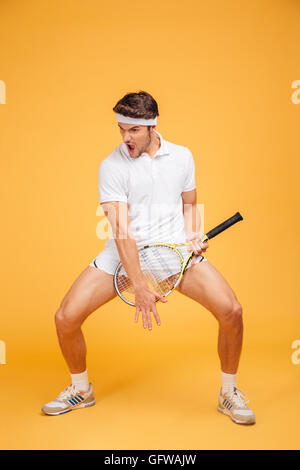 Jeune homme espiègle drôles avec joueur de tennis racket imitant la guitare sur fond jaune Banque D'Images