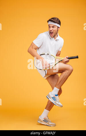 Jeune homme comique avec joueur de tennis racket de crier et de plaisanter sur fond jaune Banque D'Images