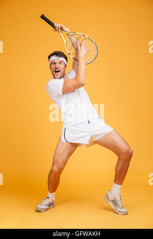 Jeune homme espiègle comique avec joueur de tennis racket en criant et en s'amusant sur fond jaune Banque D'Images