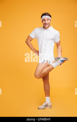 Cheerful young sportsman debout et l'étirement jambes sur fond jaune Banque D'Images