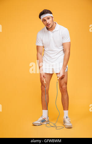 Portrait d'un jeune beau sportif fatigué tenant la corde à sauter isolé sur fond orange Banque D'Images