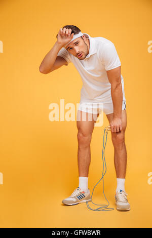 Portrait d'un jeune beau sportif fatigué tenant la corde à sauter isolé sur fond orange Banque D'Images