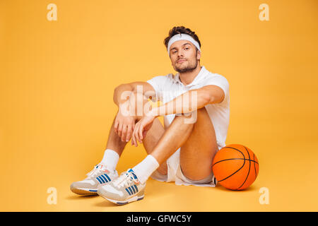 Jeune homme remise en forme reposant sur le plancher isolé sur un fond orange et looking at camera Banque D'Images