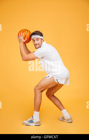 Portrait d'un beau jeune homme concentré jouer au basket-ball isolé sur un fond orange Banque D'Images