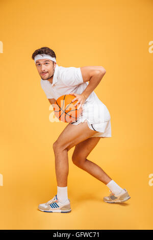 Portrait d'un beau jeune homme jouant au basket-ball isolé sur un fond orange Banque D'Images