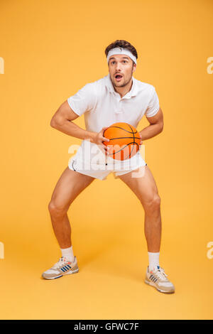 Portrait d'un beau jeune homme jouant au basket-ball isolé sur un fond orange Banque D'Images