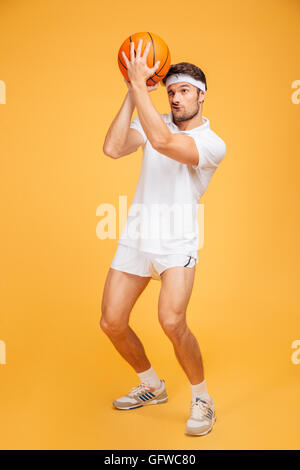 Portrait d'un beau jeune homme concentré jouer au basket-ball isolé sur un fond orange Banque D'Images